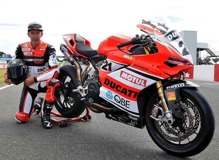 Troy Bayliss kneeling next to his race bike